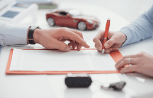 Image of agent showing client paperwork, model car and home in background, key fob in foreground.