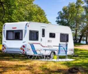 RV in front of pond or lake with chairs in front.
